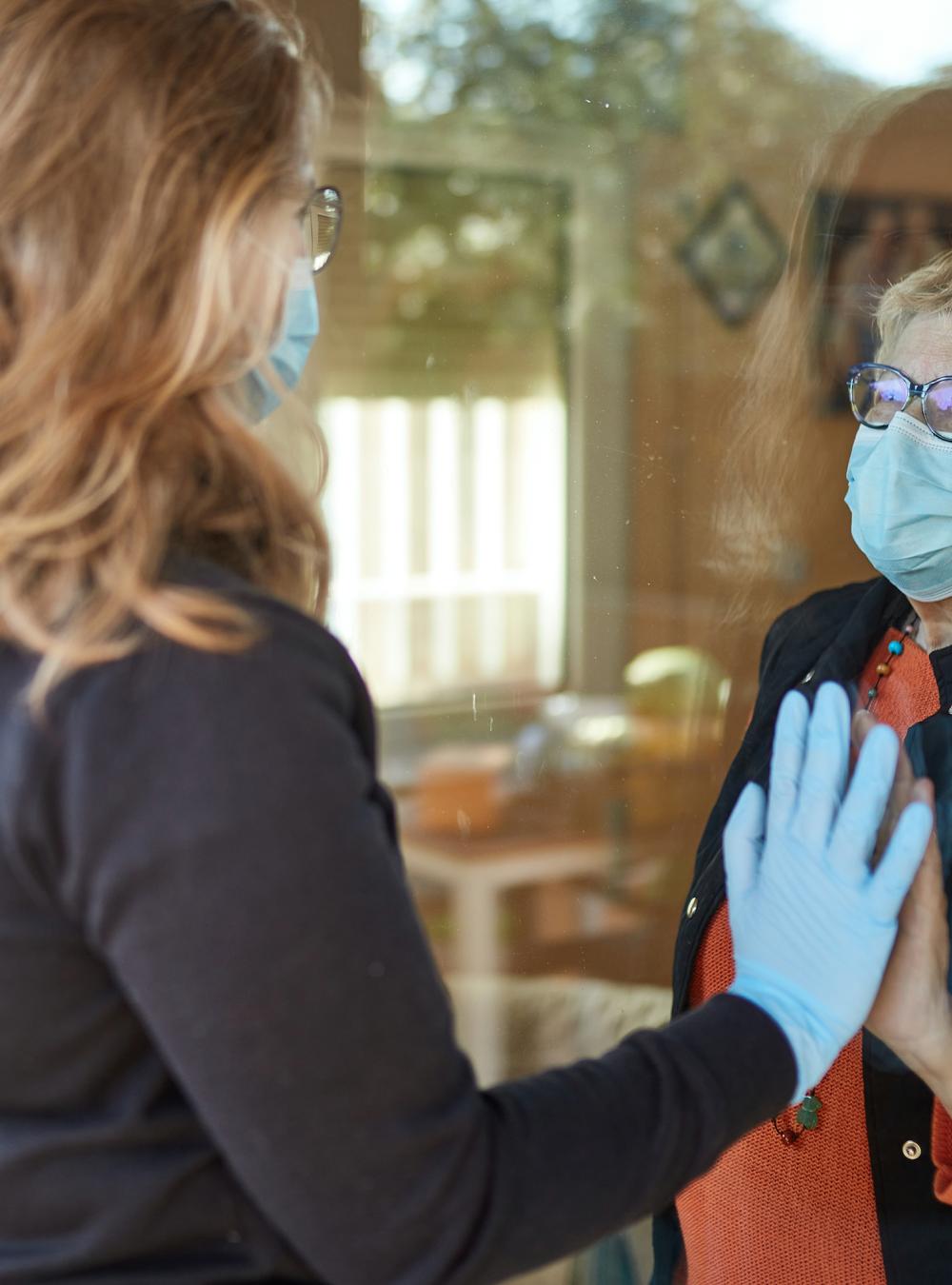 Nursing home visit with an older woman and younger woman separated by glass 