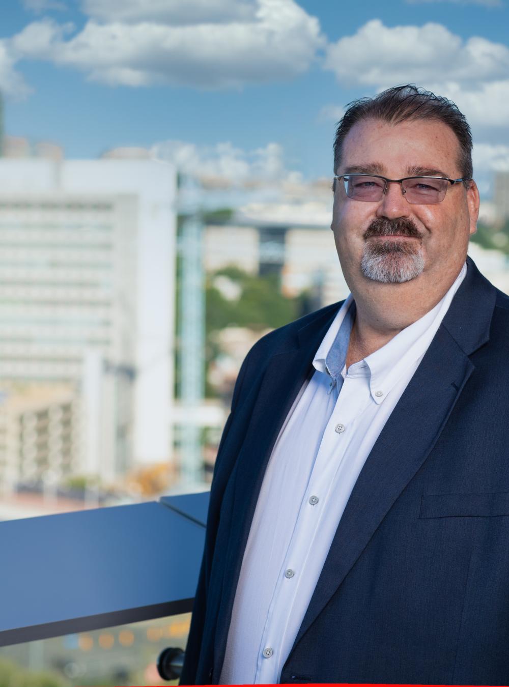 Pete Leroy on MITRE's McLean campus on a balcony overlooking the Tysons area