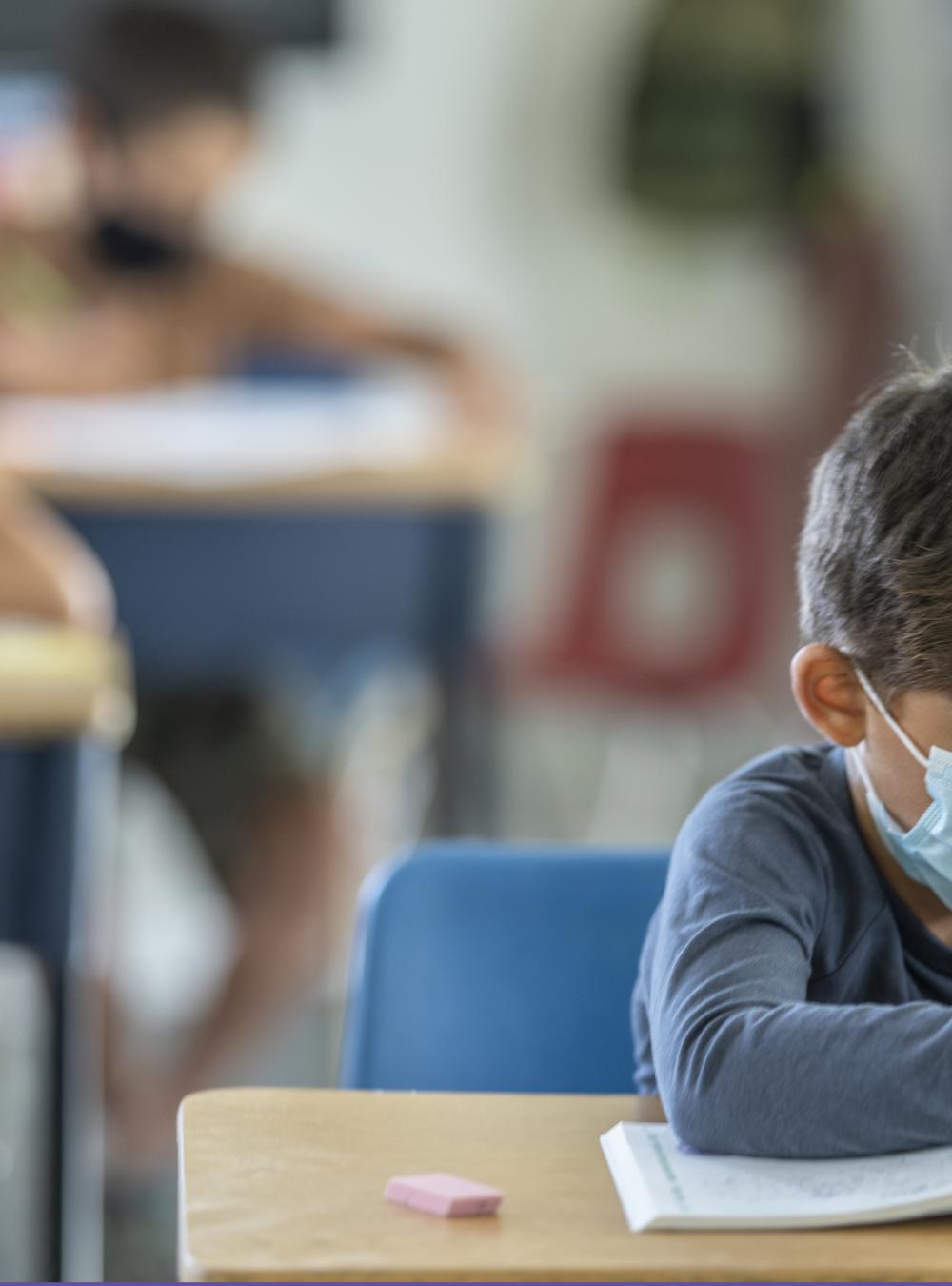 Elementary school students in a classroom wearing masks while writing in workbooks at their desks