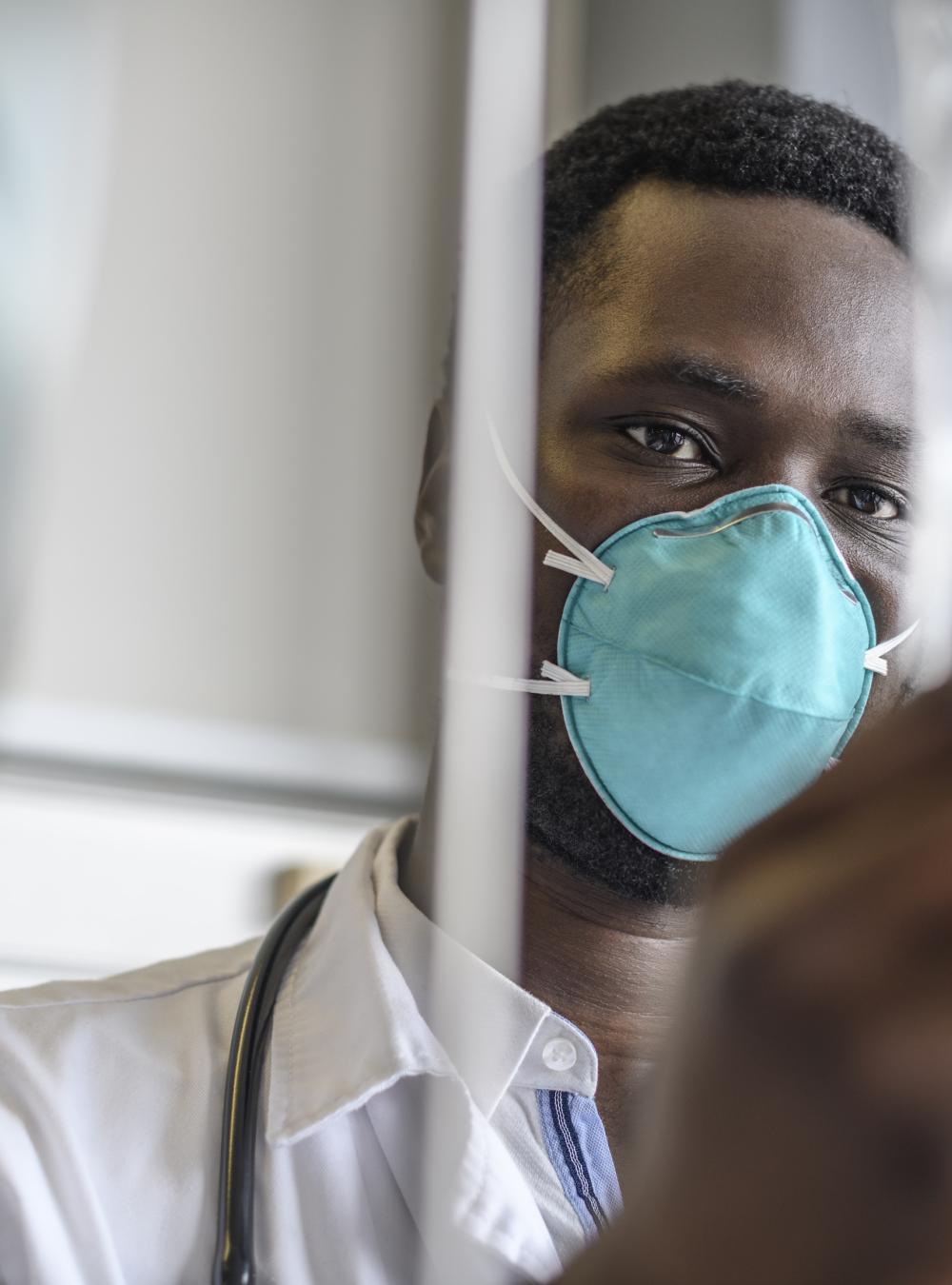 Doctor in a mask checks and IV bag in a hospital room