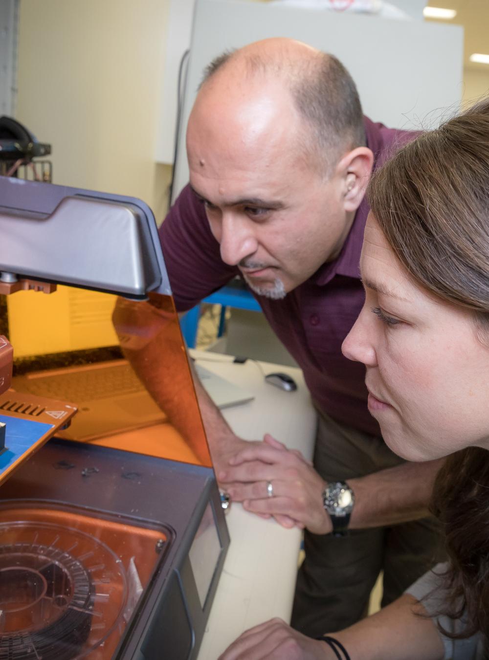 Two MITRE employees using a 3D printer