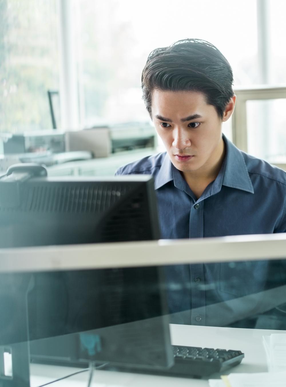 Viewed through glass, an employee with an invisible disability works at a computer in his office