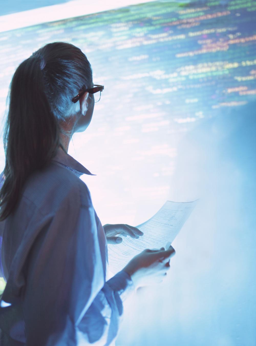 Woman standing up reviewing a large screen of code