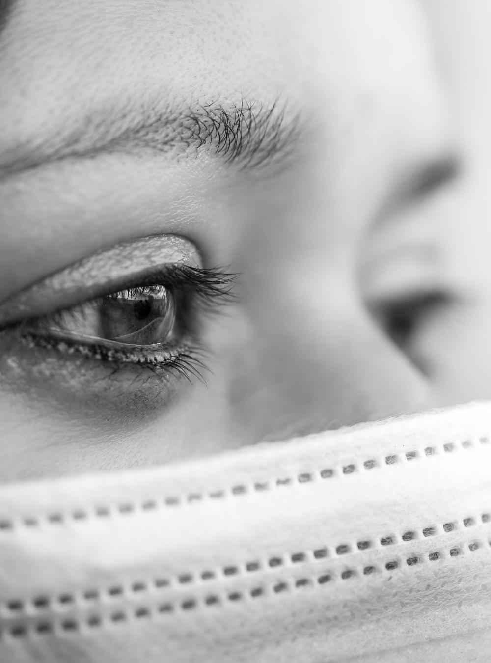 Black and white closeup of a woman in a mask, looking forward pensively