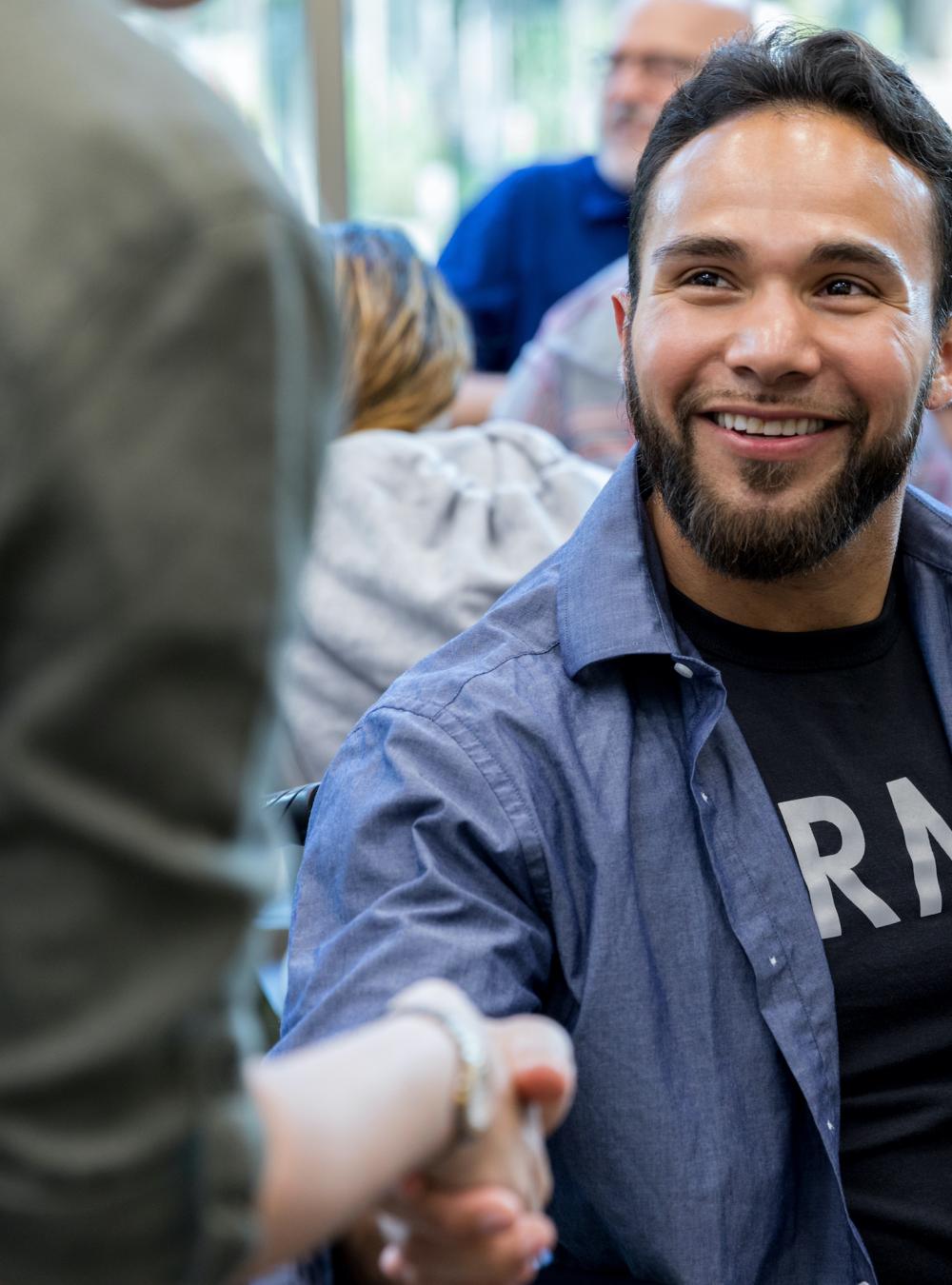 Veteran in an Army shirt shaking hands with a fellow attendee at a group meeting