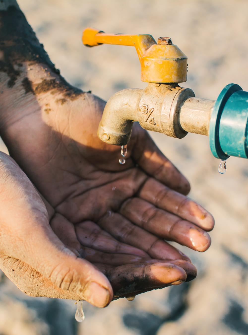 Person with dirt-caked hands catches drops of water from an outdoor faucet