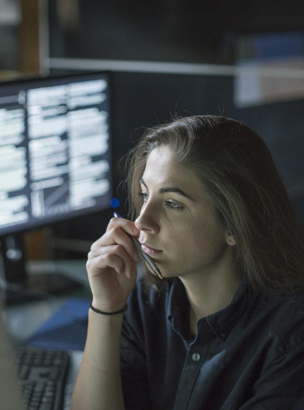 Woman carefully reviewing data while surrounded by lit up monitors