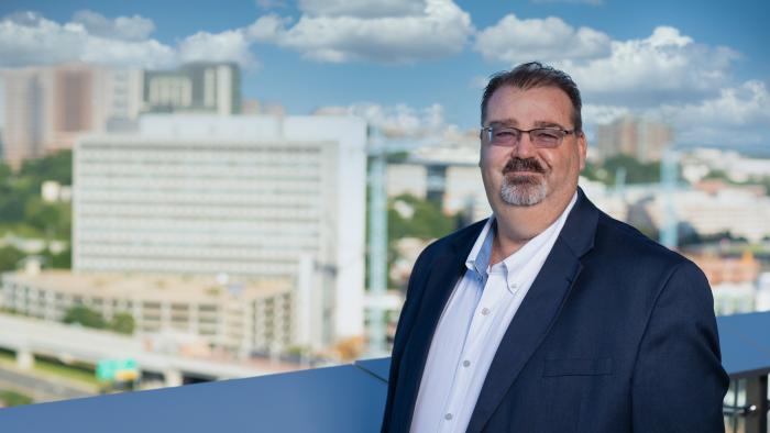 Pete Leroy on MITRE's McLean campus on a balcony overlooking the Tysons area