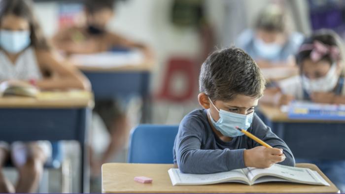 Elementary school students in a classroom wearing masks while writing in workbooks at their desks