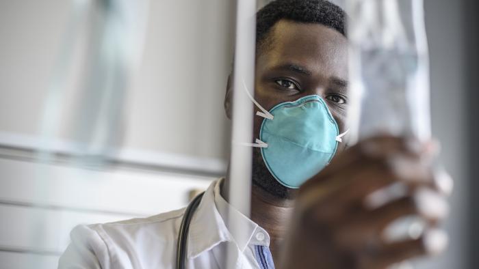 Doctor in a mask checks and IV bag in a hospital room