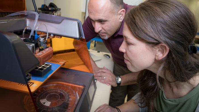 Two MITRE employees using a 3D printer