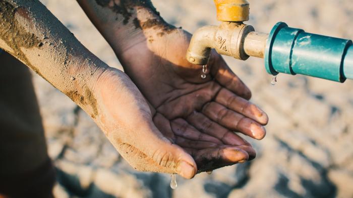 Person with dirt-caked hands catches drops of water from an outdoor faucet