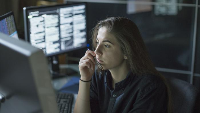 Woman carefully reviewing data while surrounded by lit up monitors