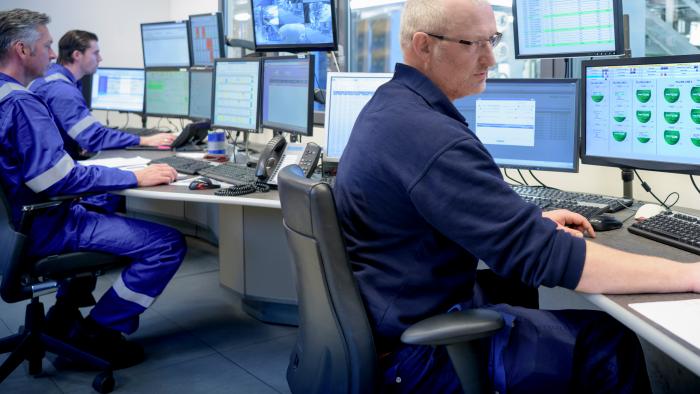 Workers in a control room surrounded by computer monitors