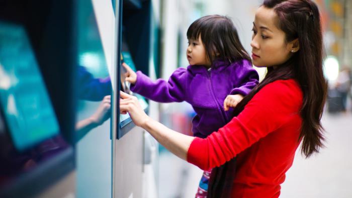 Mother and daughter using a banking machine outside