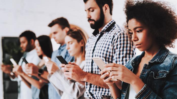 Row of standing people looking at mobile phones