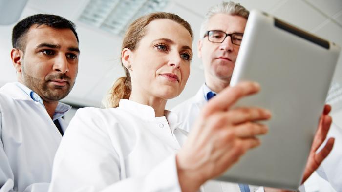 Three scientists in a laboratory, using a tablet