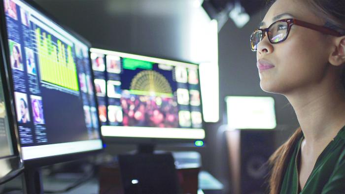 Woman sitting at her desk surrounded by 3 large computer monitors