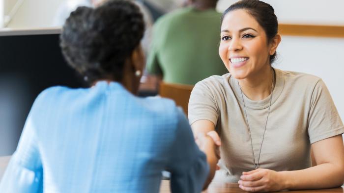 Female soldier shaking hands with a woman while sitting at a table