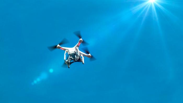 A drone with camera flying against a blue sky