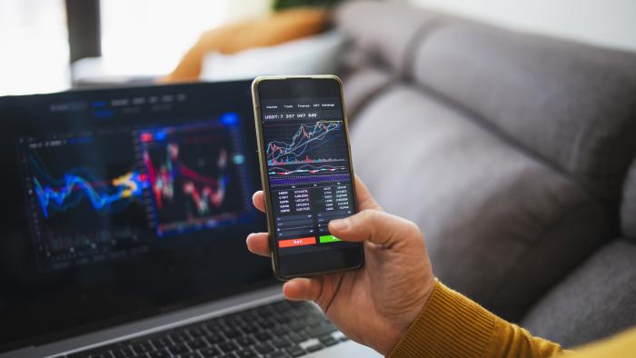 person looking at stock market on mobile phone and laptop