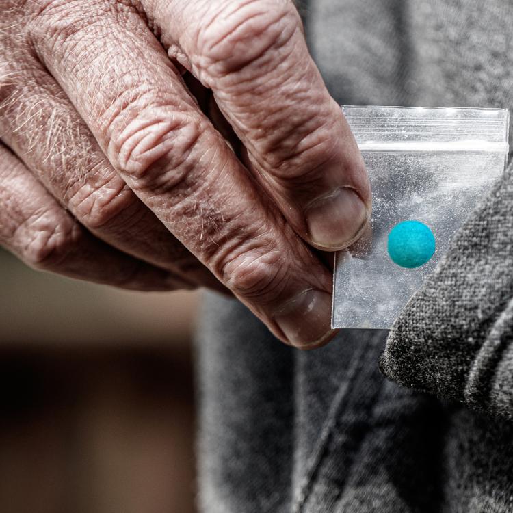 hand holding a baggie with a pill